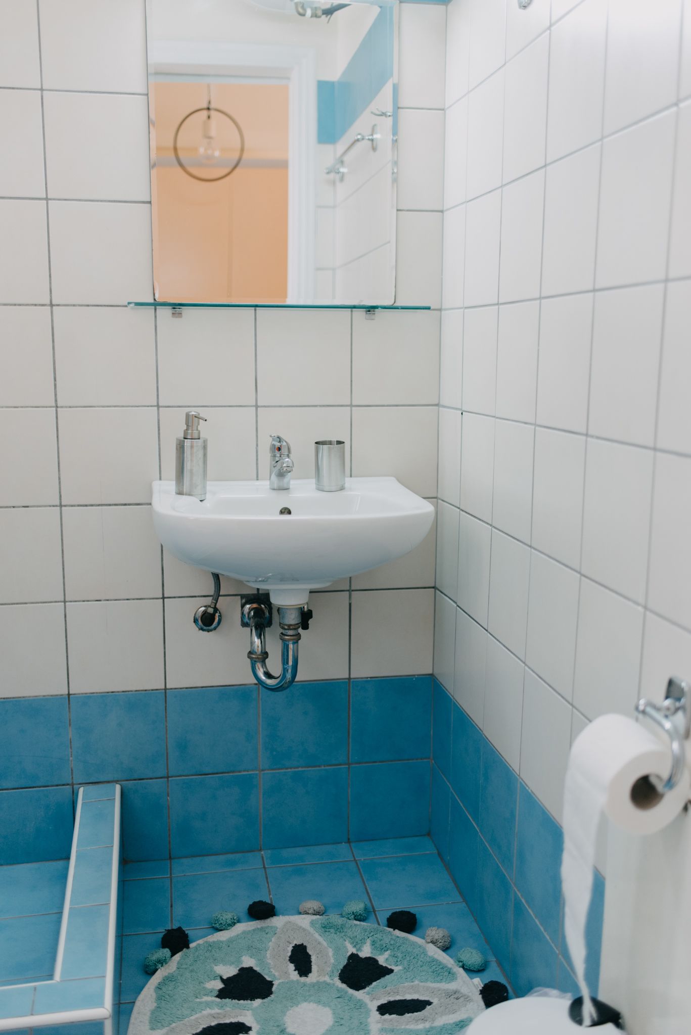Kylpyhuone, jossa on valkoinen pesuallas, siniset laatat, lasihylly ja wc-paperiteline.
