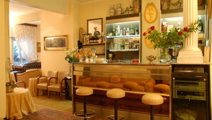 A bar area with stools, a shelf of bottles, and a vase with flowers. - Hotel Claridge (Rapallo)