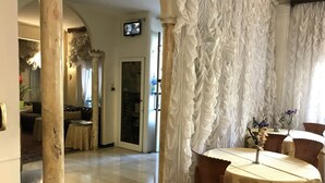 A dining area with a round table, chairs, and a decorative centerpiece. There is a television mounted on the wall and a door leading to another room. - Hotel Claridge (Rapallo)