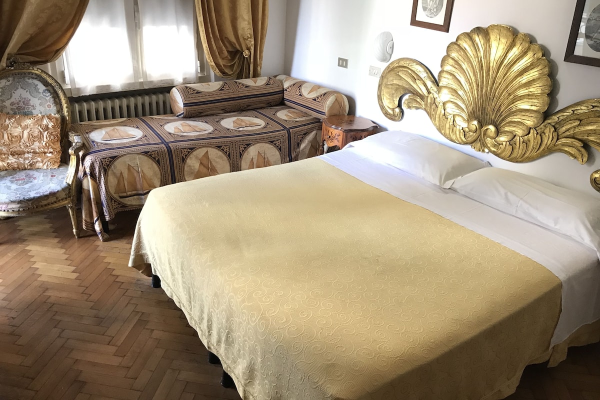 Una habitación con una cama grande, una silla, una mesita y un radiador.