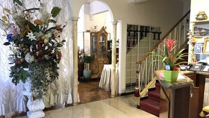A grand staircase with a red carpet, a large floral arrangement, and a vintage-style mirror in the background. - Hotel Claridge (Rapallo)