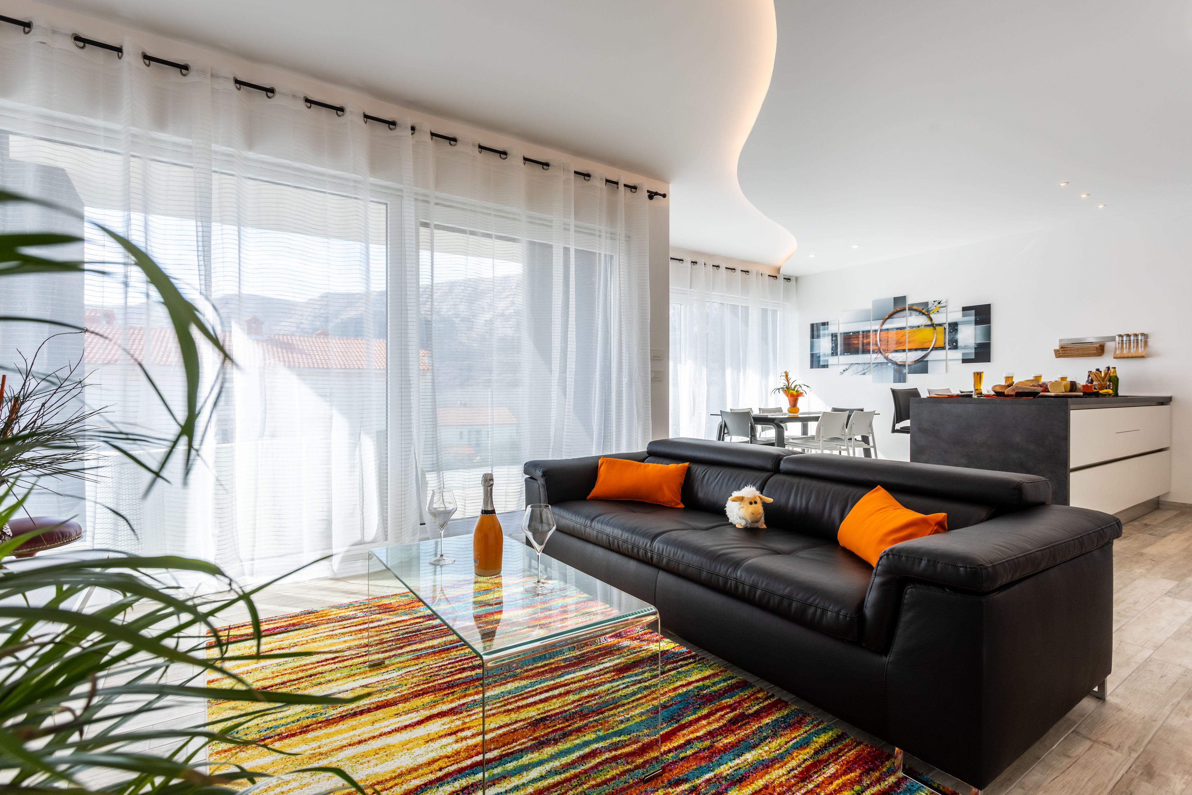 Uma sala de estar moderna com um sofá de couro preto, tapete colorido e uma mesa de centro de vidro.