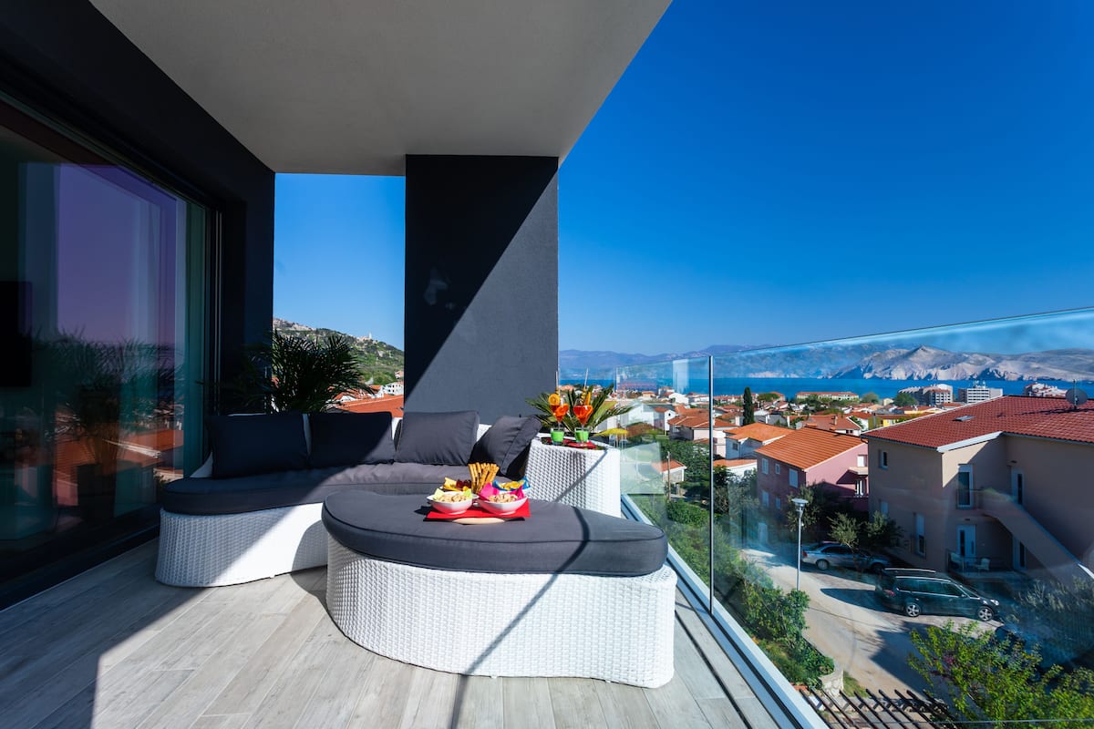 A balcony with a sofa, a small table with snacks, and a view of a cityscape and mountains.