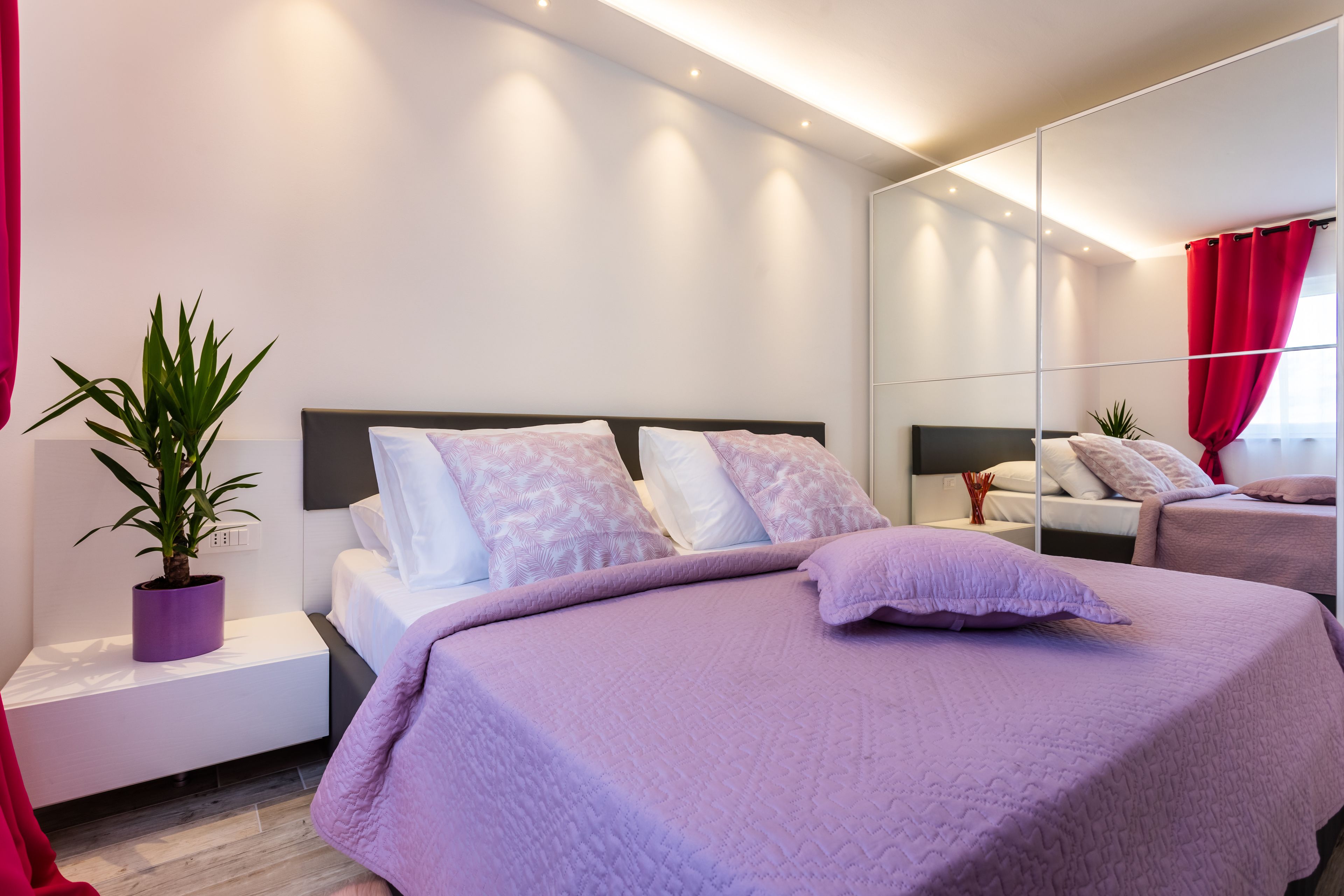 Un dormitorio moderno con una cama grande, una mesita de noche, una planta en maceta y un espejo.