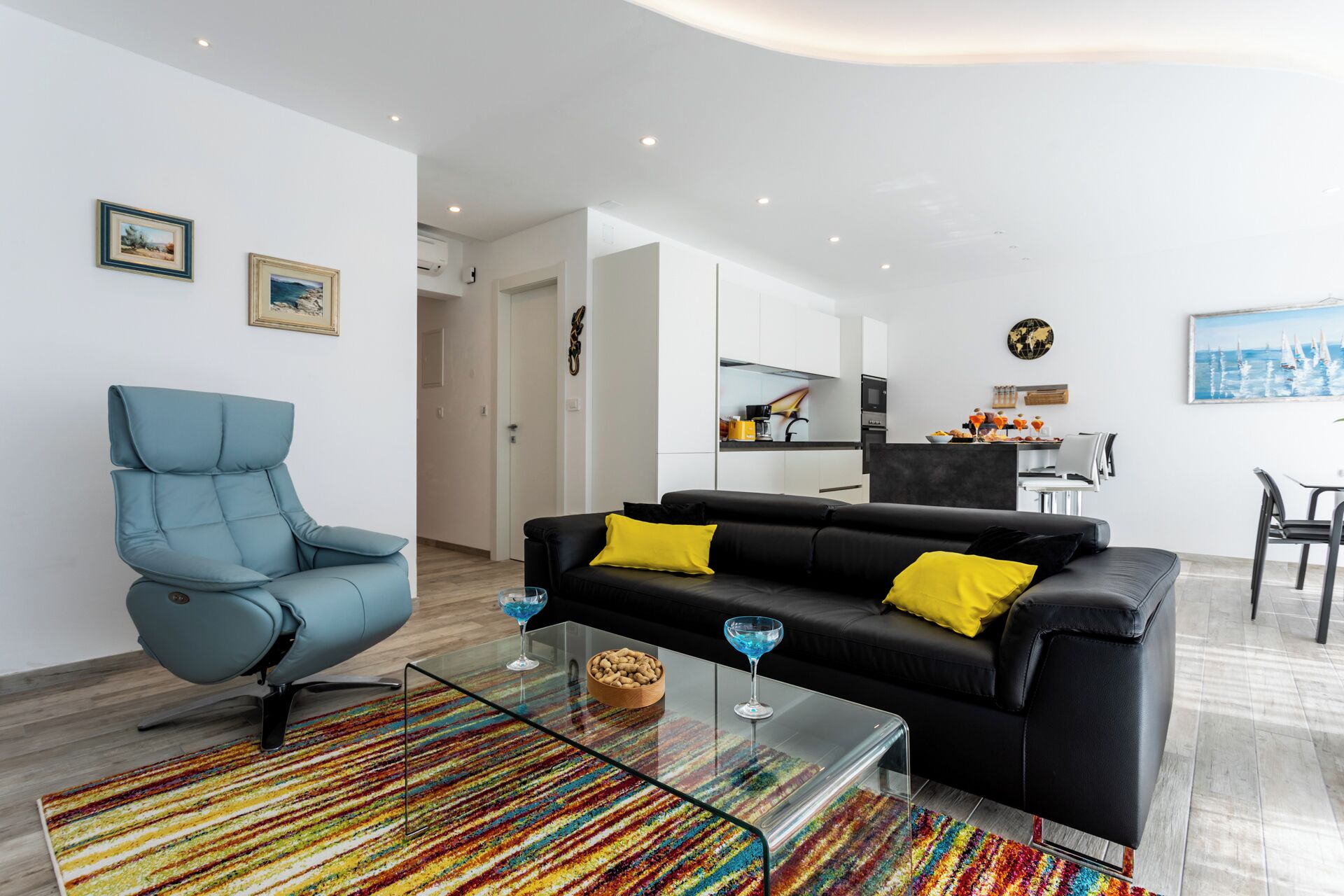 Un salon moderne avec un fauteuil bleu, un canapé noir agrémenté de coussins jaunes et une table basse en verre.