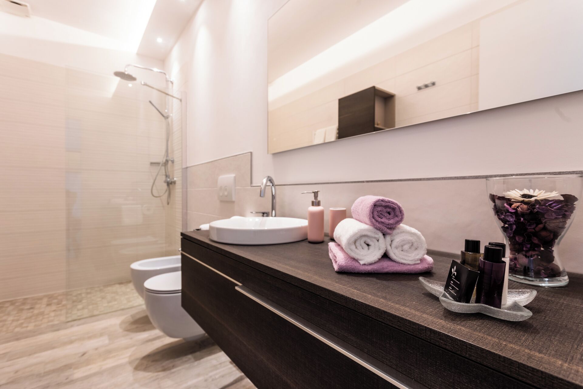 A modern bathroom with a dark wood vanity, a white sink, and a glass shower enclosure.