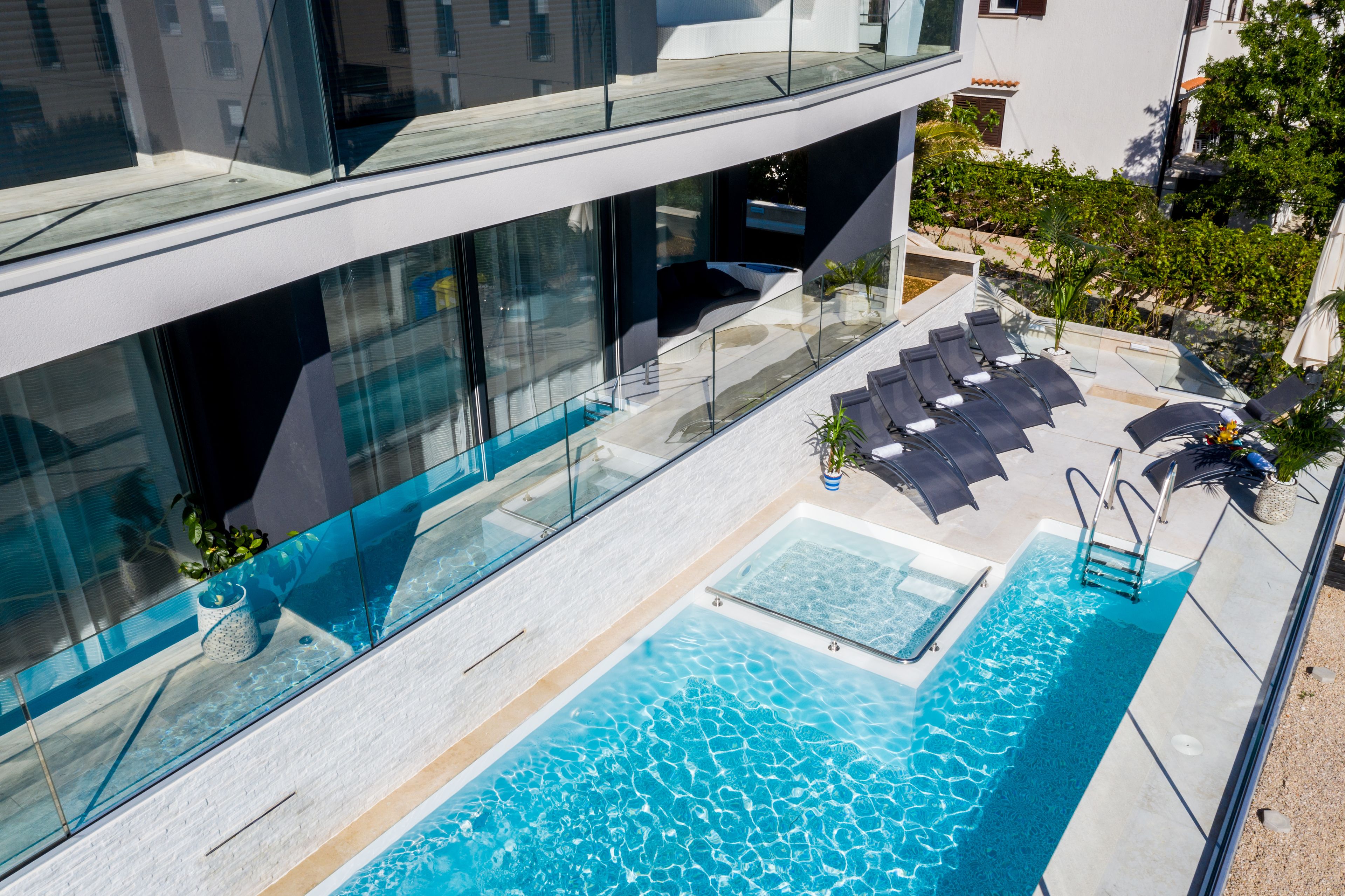 Een zwembadterras met glazen balustrades, ligbedden en een klein zwembad.