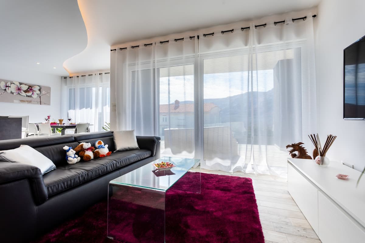 A modern living room with a black leather sofa, a glass coffee table, and a red rug.