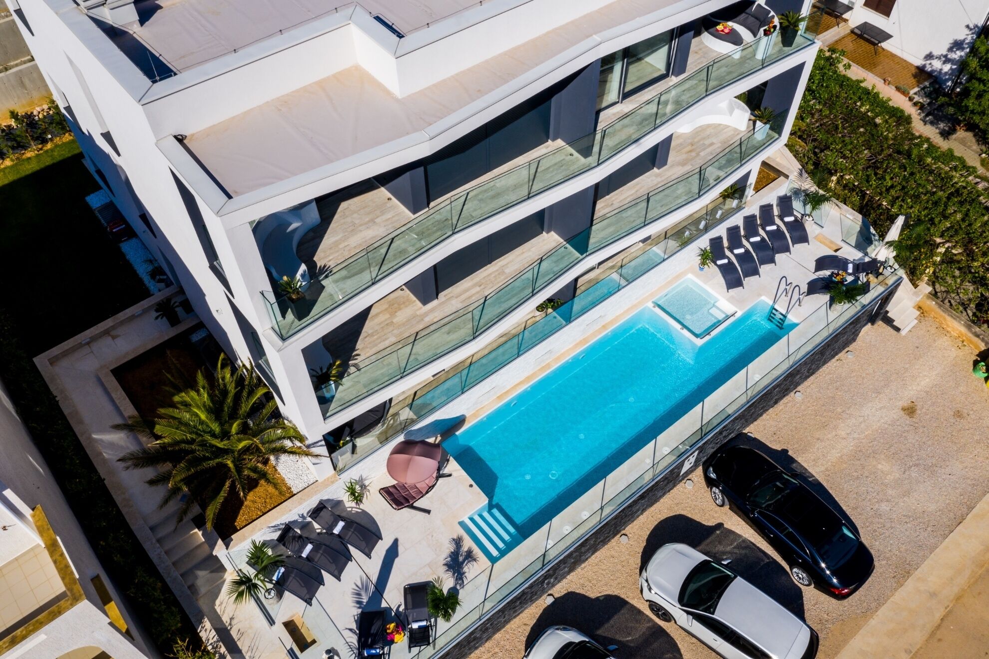 Un edificio moderno de varios pisos con piscina en la azotea, zona de estar al aire libre y cochera.
