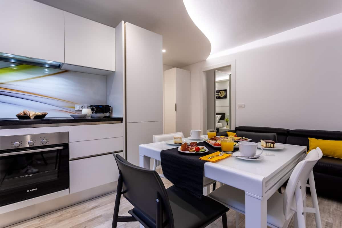 A modern kitchen with a dining area, featuring a Bosch oven, white cabinets, and a black chair.