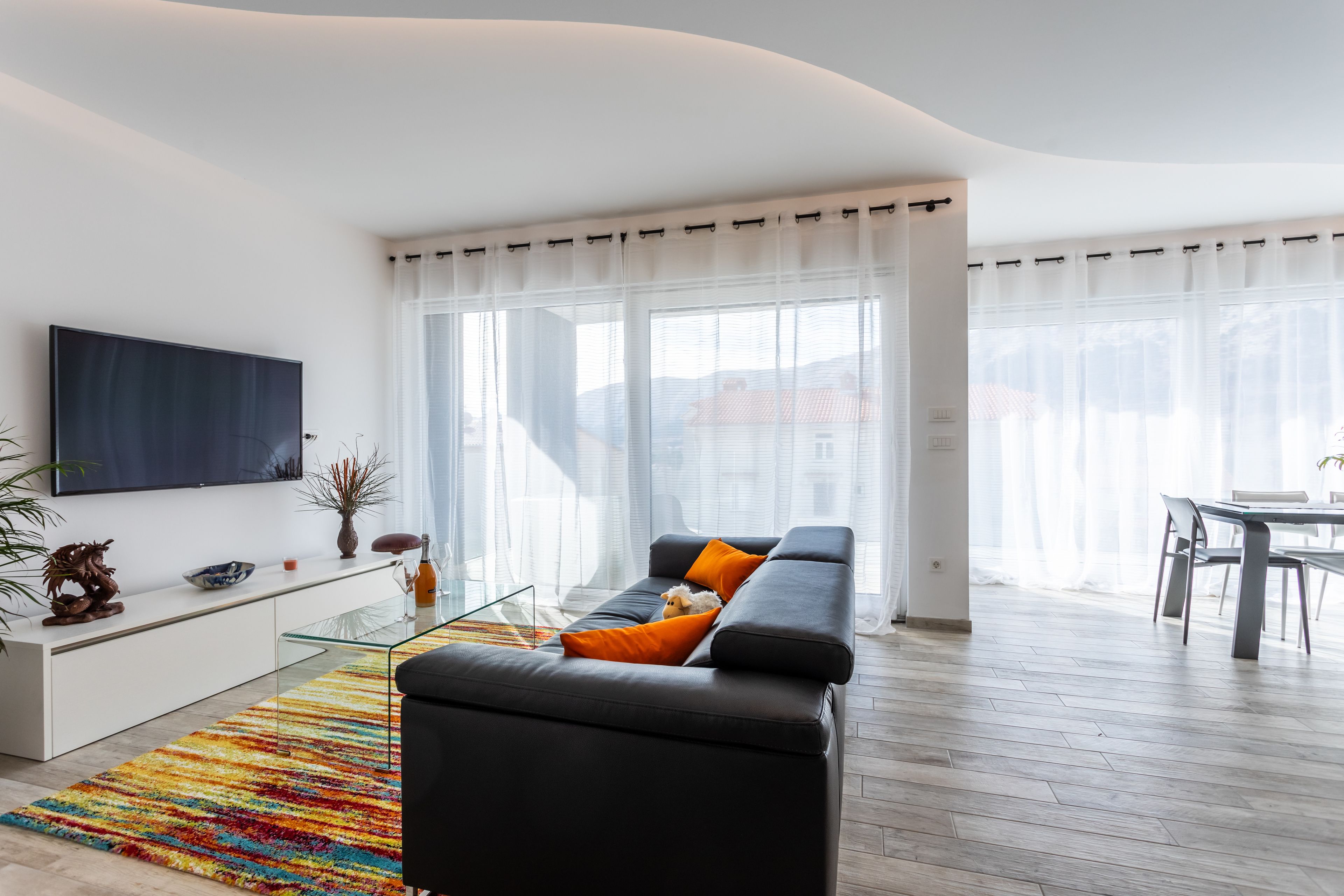 A modern living room with a black sofa, a flat-screen TV, and a dining area with a table and chairs.