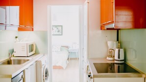 A compact kitchen with a microwave, coffee maker, and washing machine. A bed and a small table are visible in the adjacent room. - Best House Rooftop Apt Marina Zeas (Piraeus)