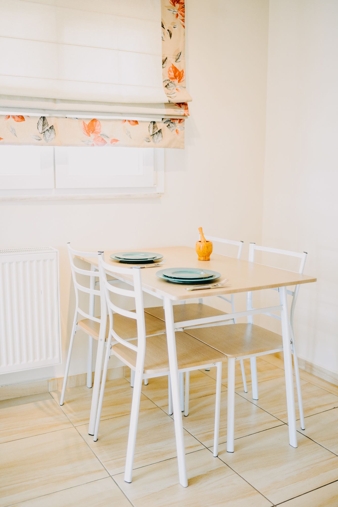 A dining table with four white chairs, a yellow vase, and plates on the table.