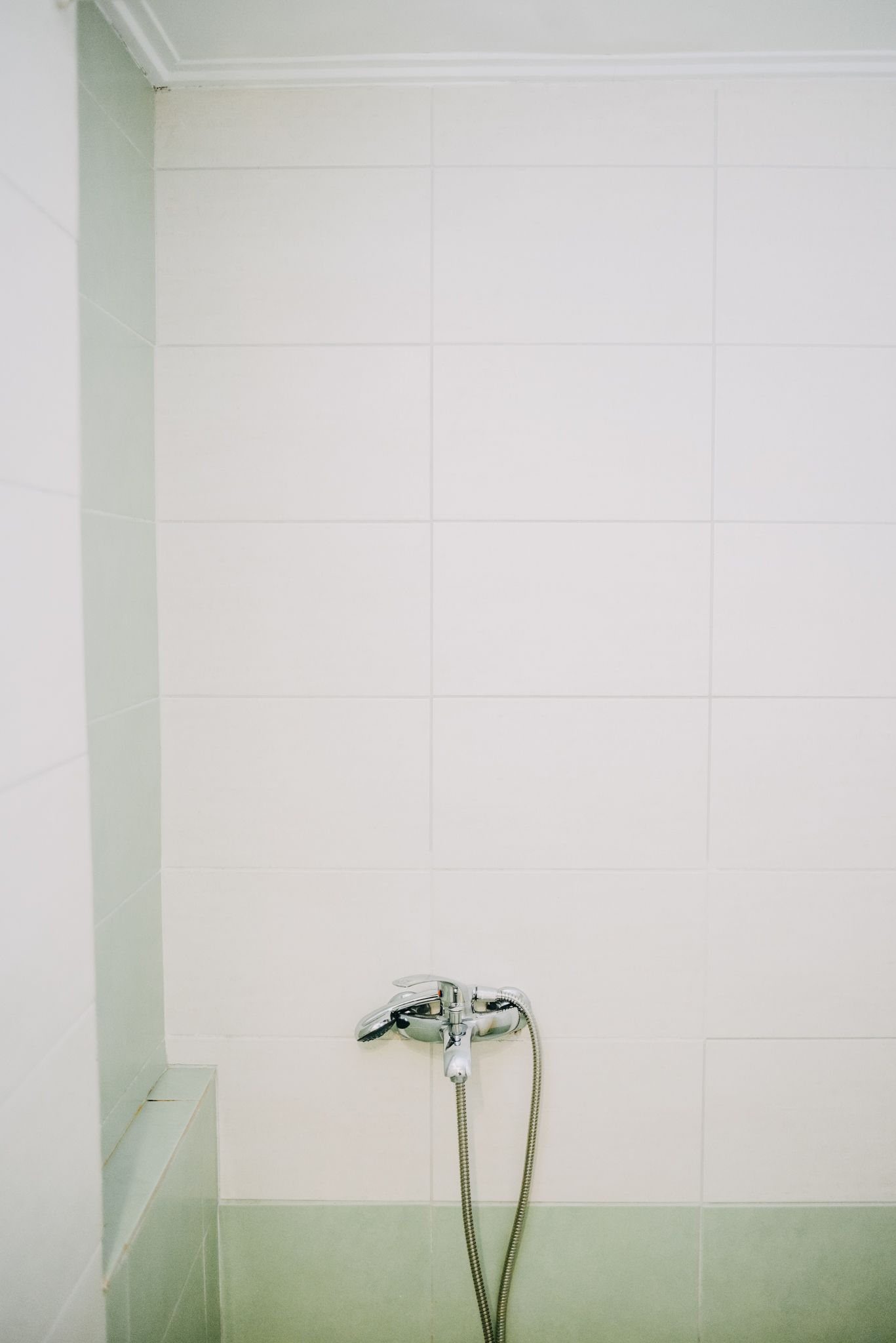 Une salle de bain avec des murs recouverts de carreaux blancs et une douche équipée d’un pommeau de douche amovible.