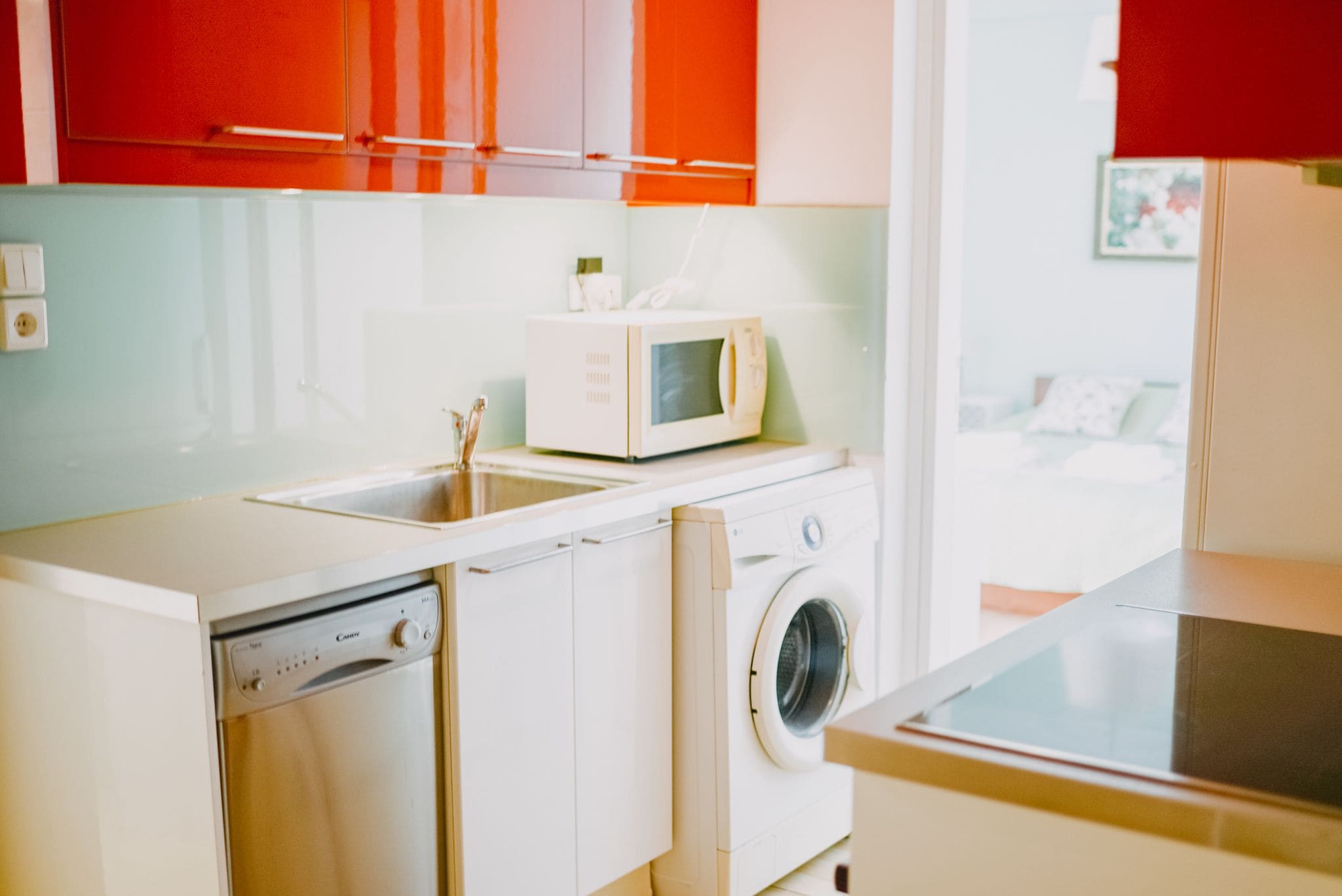 A compact kitchen with a dishwasher, washing machine, and a microwave on the countertop.