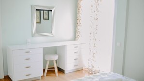 A bedroom with a white dresser, a small stool, a bed with a floral bedspread, and a wall-mounted mirror. - Best House Rooftop Apt Marina Zeas (Piraeus)