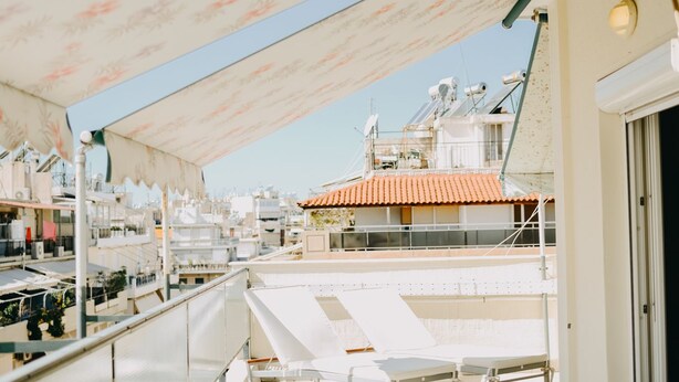 A rooftop terrace with a table and chairs, a patterned awning, and a view of buildings in the background. - Best House Rooftop Apt Marina Zeas (Piraeus)