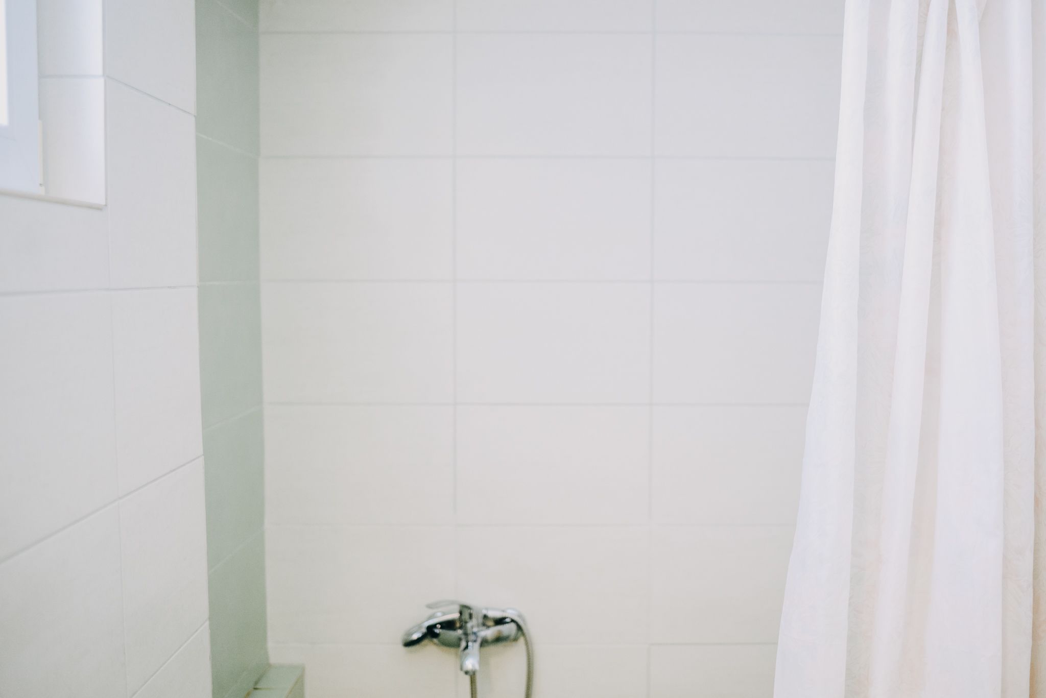 A bathroom with white tiles, a shower curtain, and a showerhead.