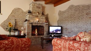 A cozy living room with a stone fireplace, red patterned sofas, and a television.