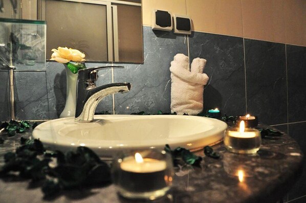 A bathroom with a round sink, a mirror, and a white towel hanging on the wall. There are candles on the countertop.