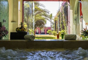 A spa room with a view of a courtyard, a bathtub, and a fruit bowl on the windowsill.