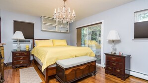 A bedroom with a bed, a bench, a dresser, a nightstand, a chandelier, and a window with blinds.