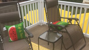 A deck with two wicker chairs, one with a watermelon pillow, and a small table.