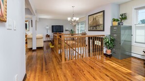 A spacious living room with a wooden staircase, a flat-screen TV, and a large painting on the wall.