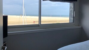 Une pièce dotée d’une grande fenêtre donnant sur la plage et un voilier.