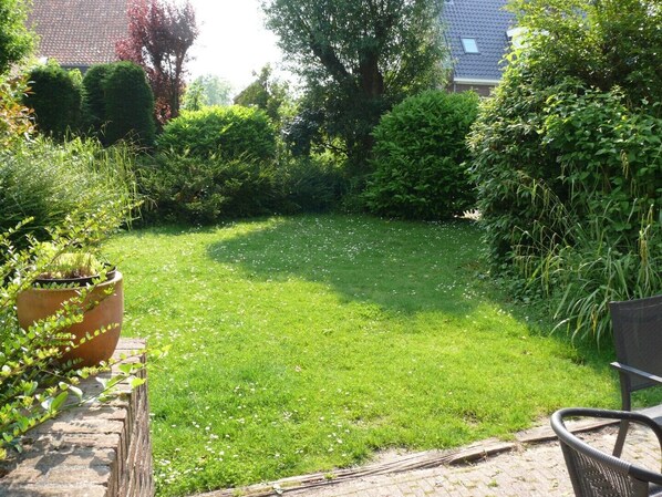 A well-maintained garden with a lawn, a large planter, and a wicker chair. - Comfortable 8-person holiday home in a quiet location on 530 m² of land (Scharendijke)