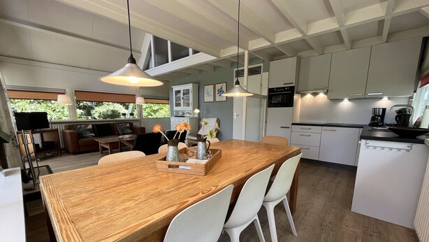 Une cuisine moderne avec des meubles blancs, une table à manger en bois et des luminaires suspendus.
