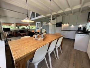 A modern kitchen with white cabinets, a wooden dining table, and pendant lights. - Comfortable 8-person holiday home in a quiet location on 530 m² of land (Scharendijke)