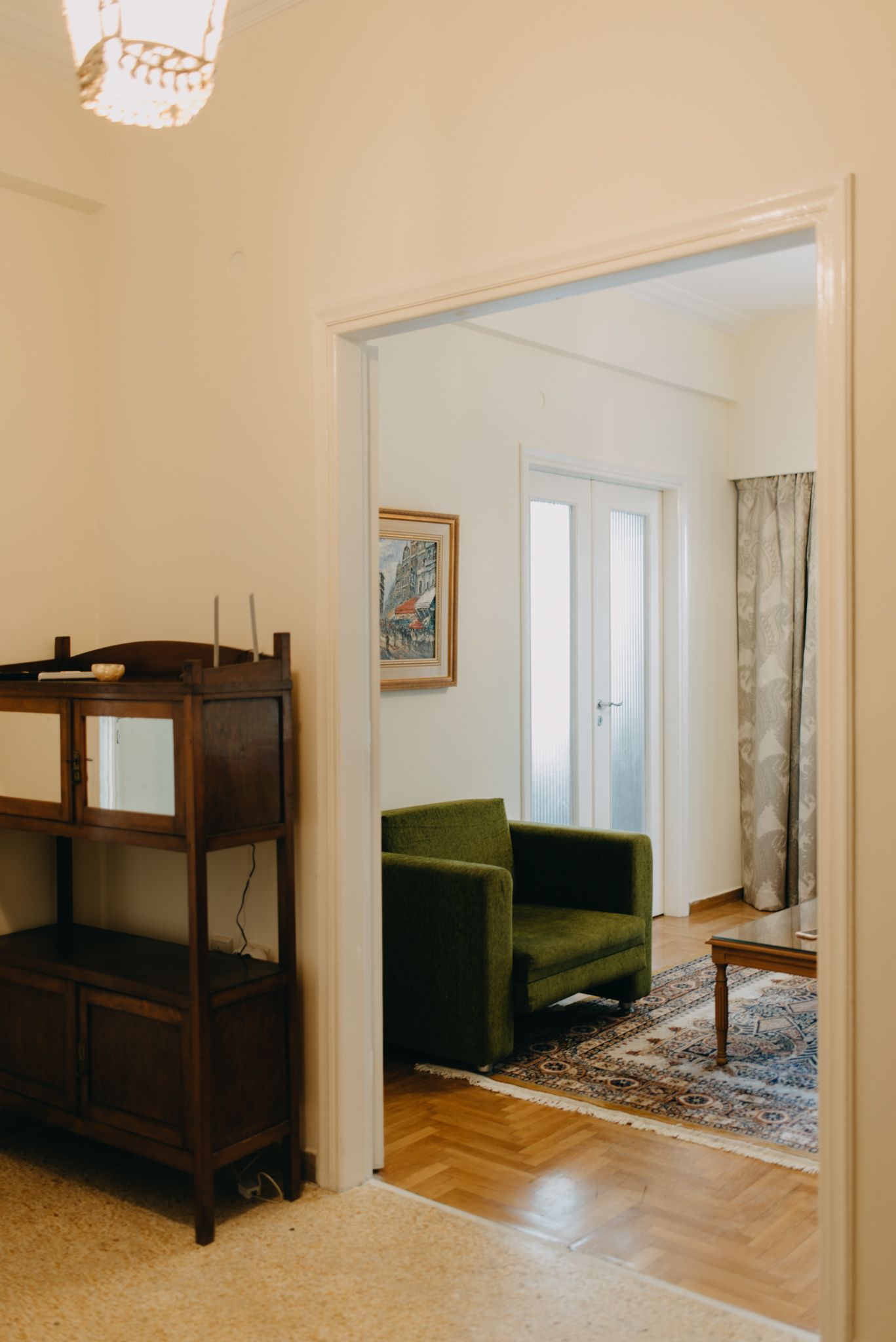 Una habitación con un armario de madera, un sillón verde, un tapete estampado y un cuadro en la pared.