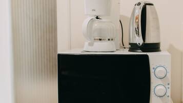 Un microondas Samsung sobre un electrodoméstico blanco, con una cafetera y un hervidor encima.