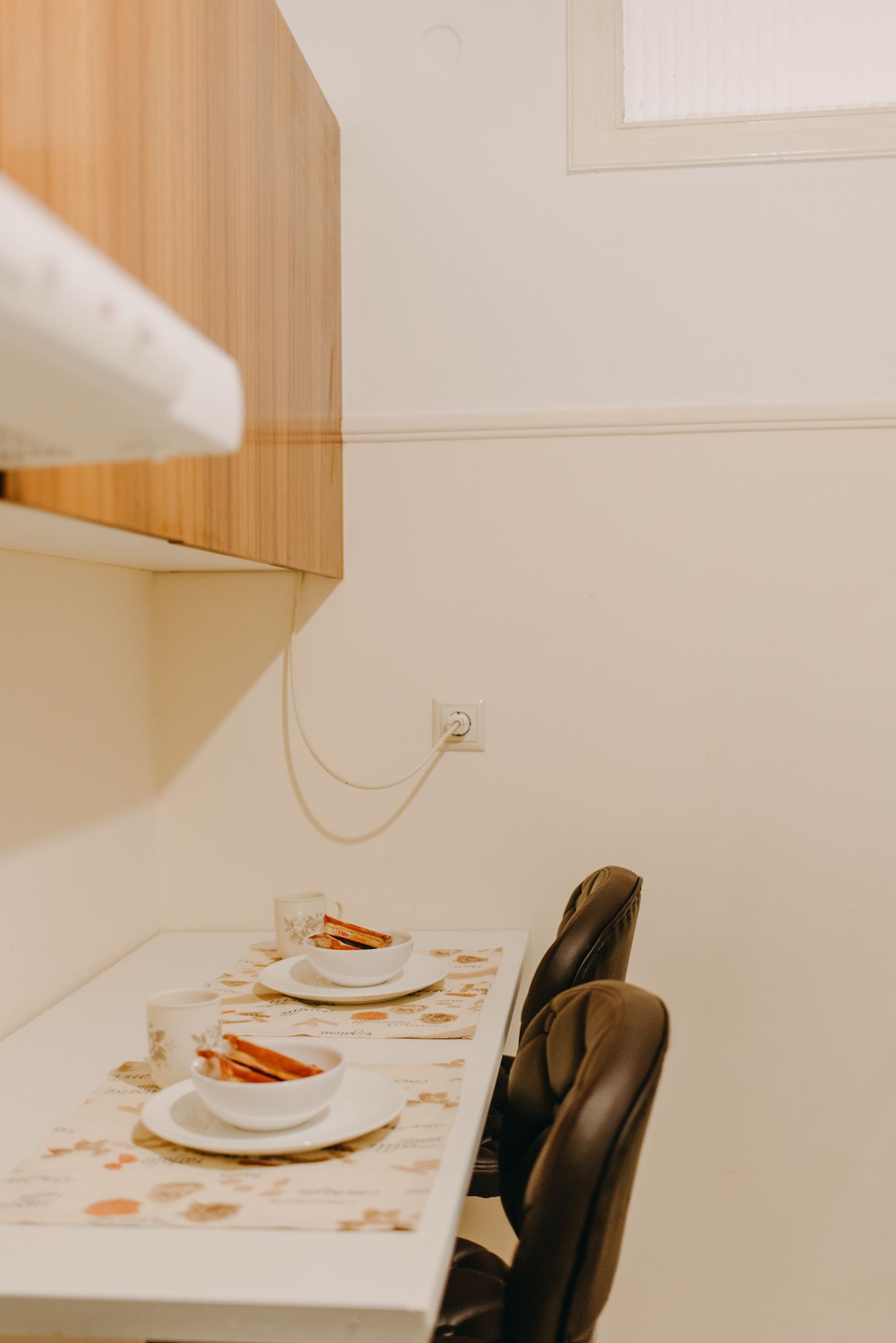 Een eettafel met twee borden en bekers, een stopcontact op de muur, en een houten kast erboven.