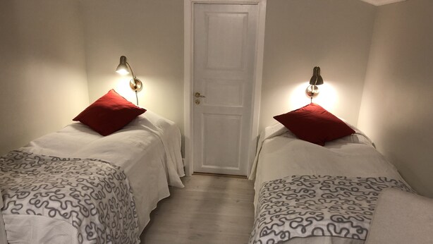 Une chambre avec deux lits, chacun agrémenté d’un oreiller rouge et d’une couverture à motifs. Des lampes murales sont fixées au-dessus de chaque lit.