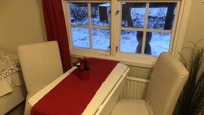 Une pièce avec une table et des chaises blanches, une fenêtre donnant sur un paysage enneigé et une plante en pot.