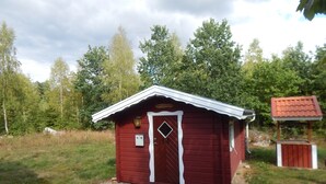 Une petite cabane en bois rouge, avec une porte blanche et un petit porche.