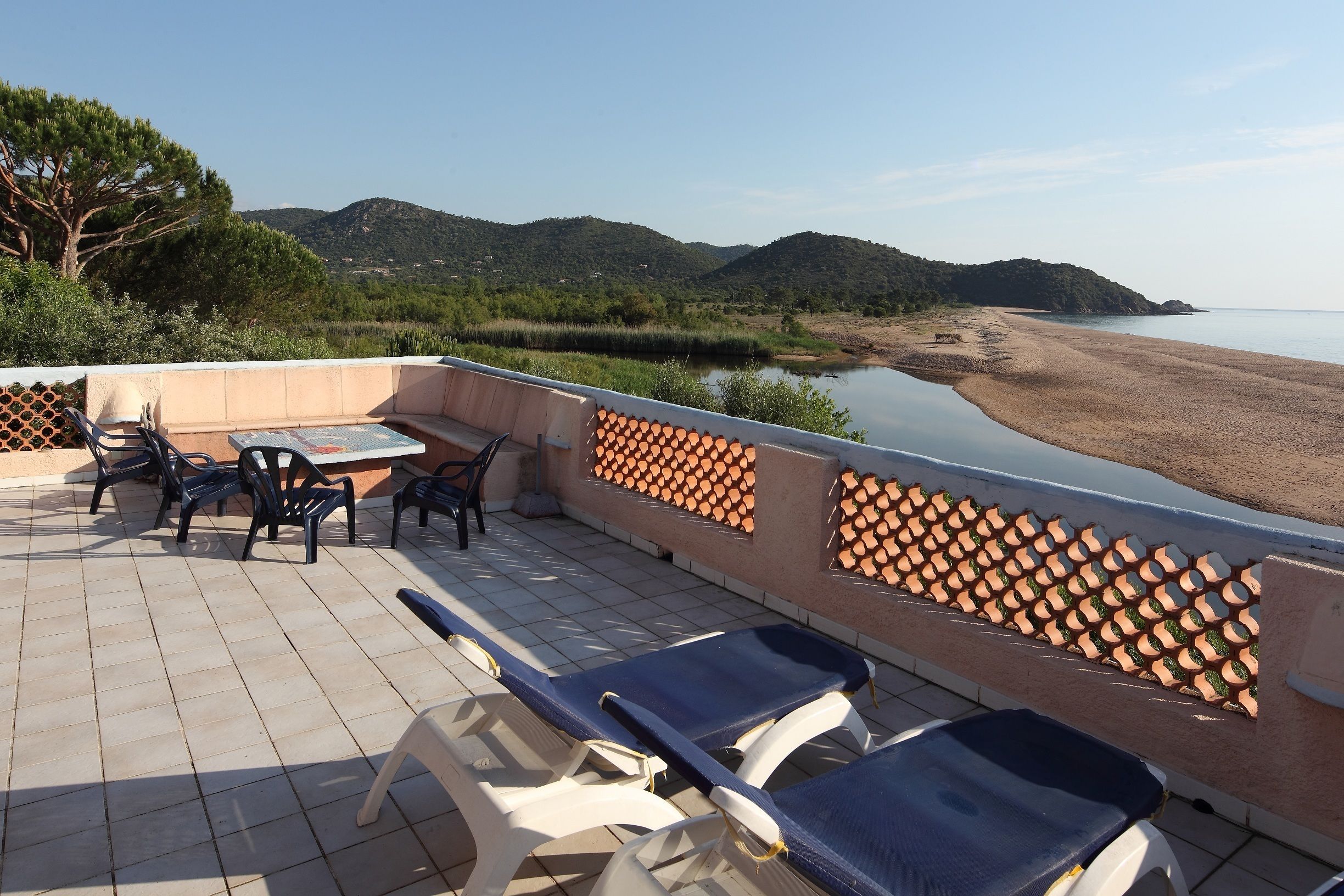 Una terraza con mesa y sillas, con vista a una playa y colinas.