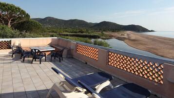 Una terraza con mesa y sillas, con vista a una playa y colinas.
