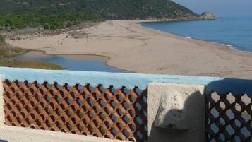 Vista costera con playa arenosa, un pequeño cuerpo de agua y una colina al fondo.