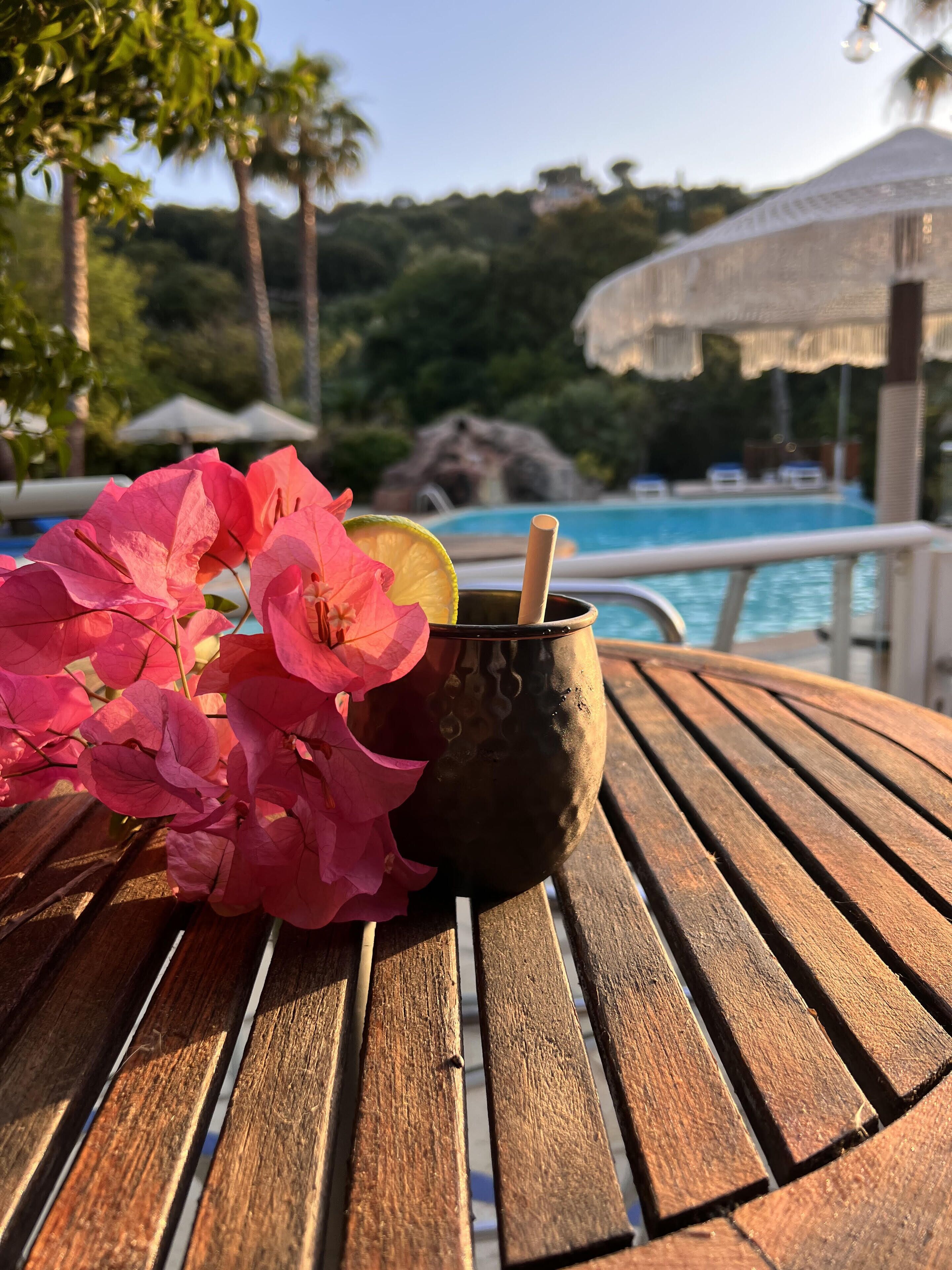 A wooden table with a drink in a black mug, a pink flower, and a slice of lime.