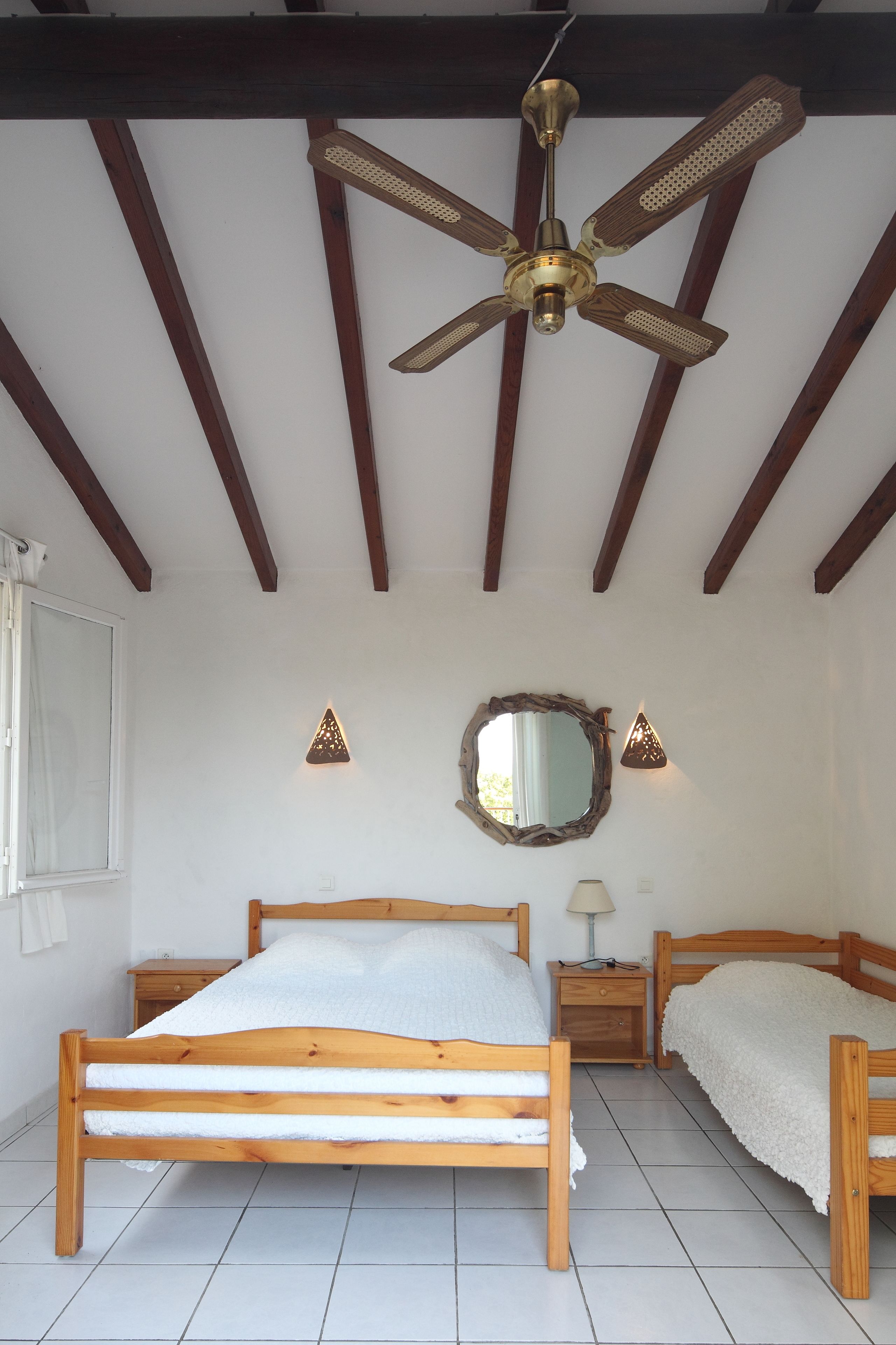 A bedroom with a wooden bed, a ceiling fan, a mirror, and a nightstand.
