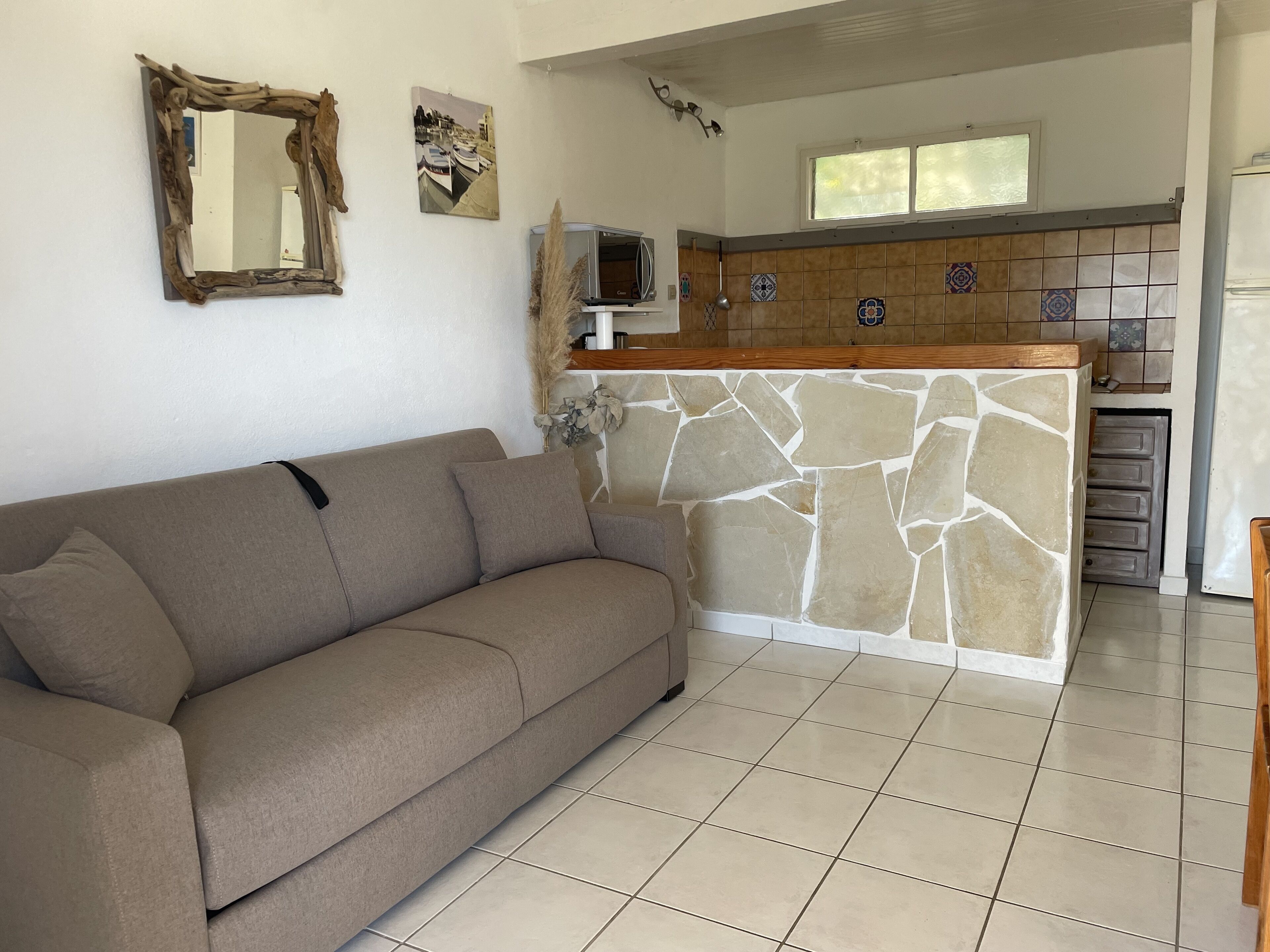 Una sala de estar con sofá, un muro de acento de piedra, una zona de cocina con salpicadero de azulejos y una ventana sobre el lavabo.