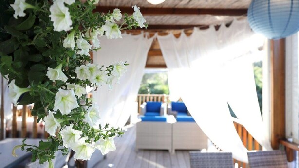 A covered outdoor seating area with white curtains and hanging flowers. - Residence Fium del Cavo (Zonza)