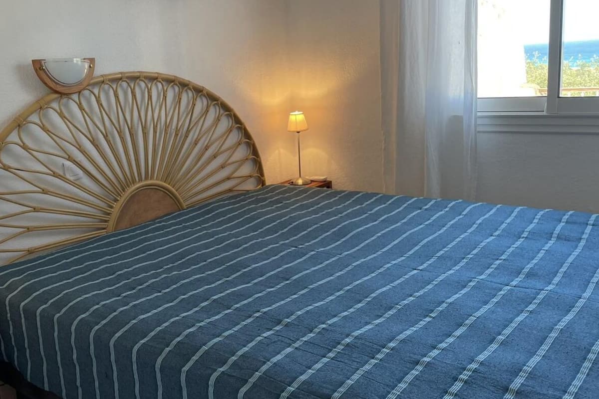 A bed with a blue striped bedspread, a wooden headboard, a bedside lamp, and a nightstand with a lamp.