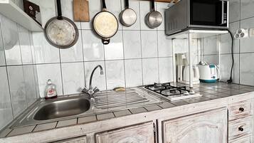 Una cocina con paredes de azulejos blancos, un lavamanos de acero inoxidable, una estufa y un microondas.