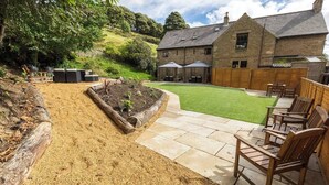 Un jardín con un patio, mobiliario exterior y un edificio de piedra al fondo.
