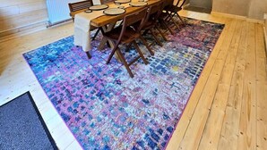 Un comedor con una mesa y sillas de madera, un tapete colorido y una pared de piedra.