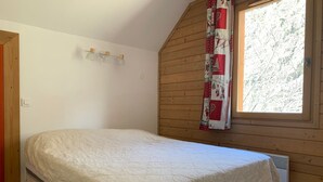 Une chambre avec un lit, une fenêtre avec un rideau et un mur en bois.